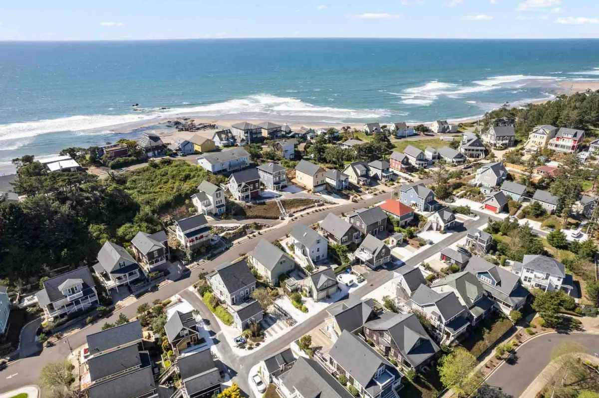A sweeping view over the Olivia Beach neighborhood, capturing the arrangement of charming houses, green spaces, and the sparkling ocean beyond. The image radiates a relaxed, community-oriented mood, hinting at outdoor gatherings, picnics in the park, and easy access to the beach.