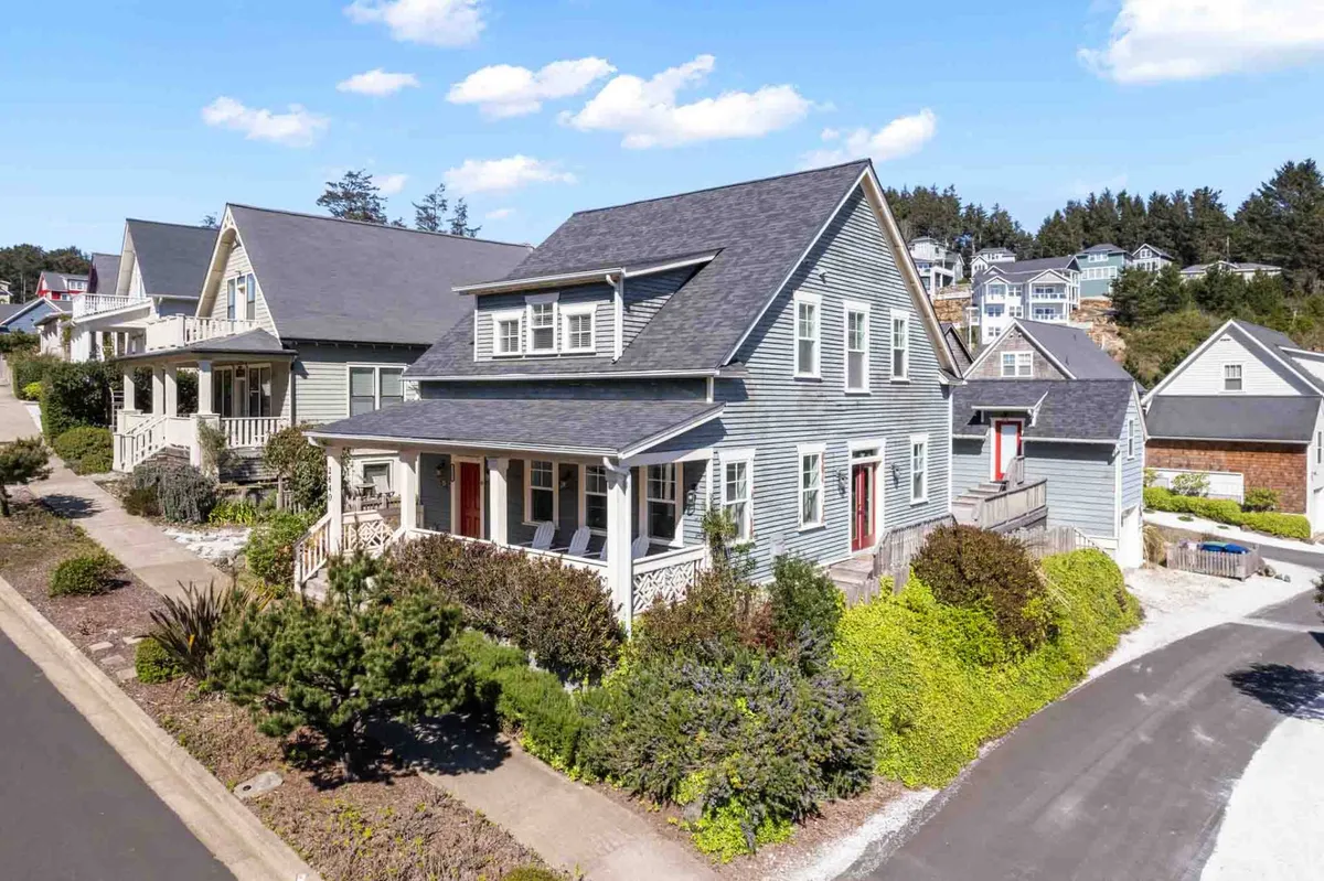 The image showcases the welcoming facade of a charming single-family beach cottage with a spacious front porch, lush landscaped garden, and warm light spilling from the windows. The porch beckons guests to relax and enjoy sunset views, all set within the friendly Olivia Beach Community.