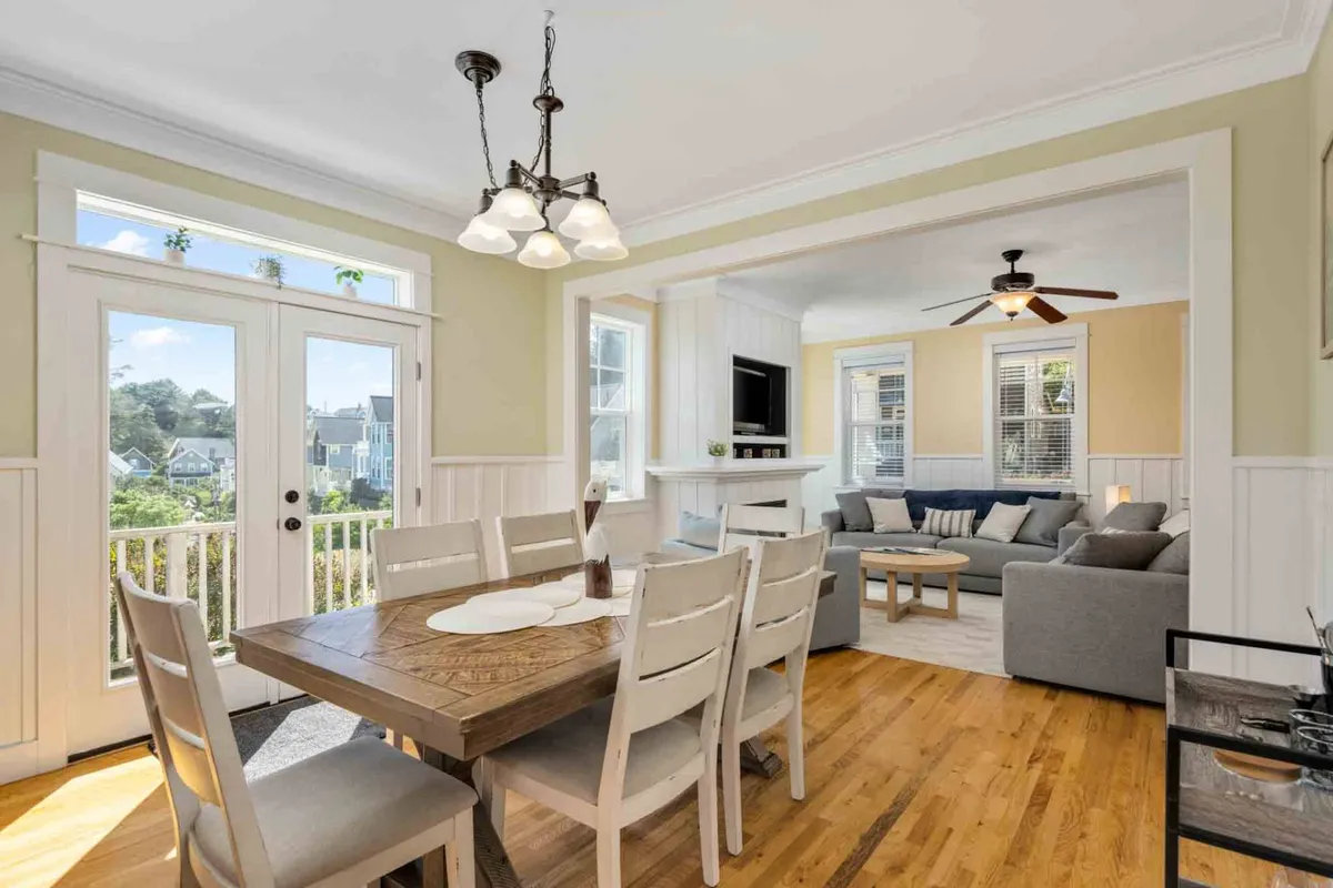 A spacious dining area flows seamlessly into a cozy living room seating space. The dining table is set for a family meal, and soft light streams through the windows. The living area features comfortable seating, creating an inviting environment for socializing or relaxing.
