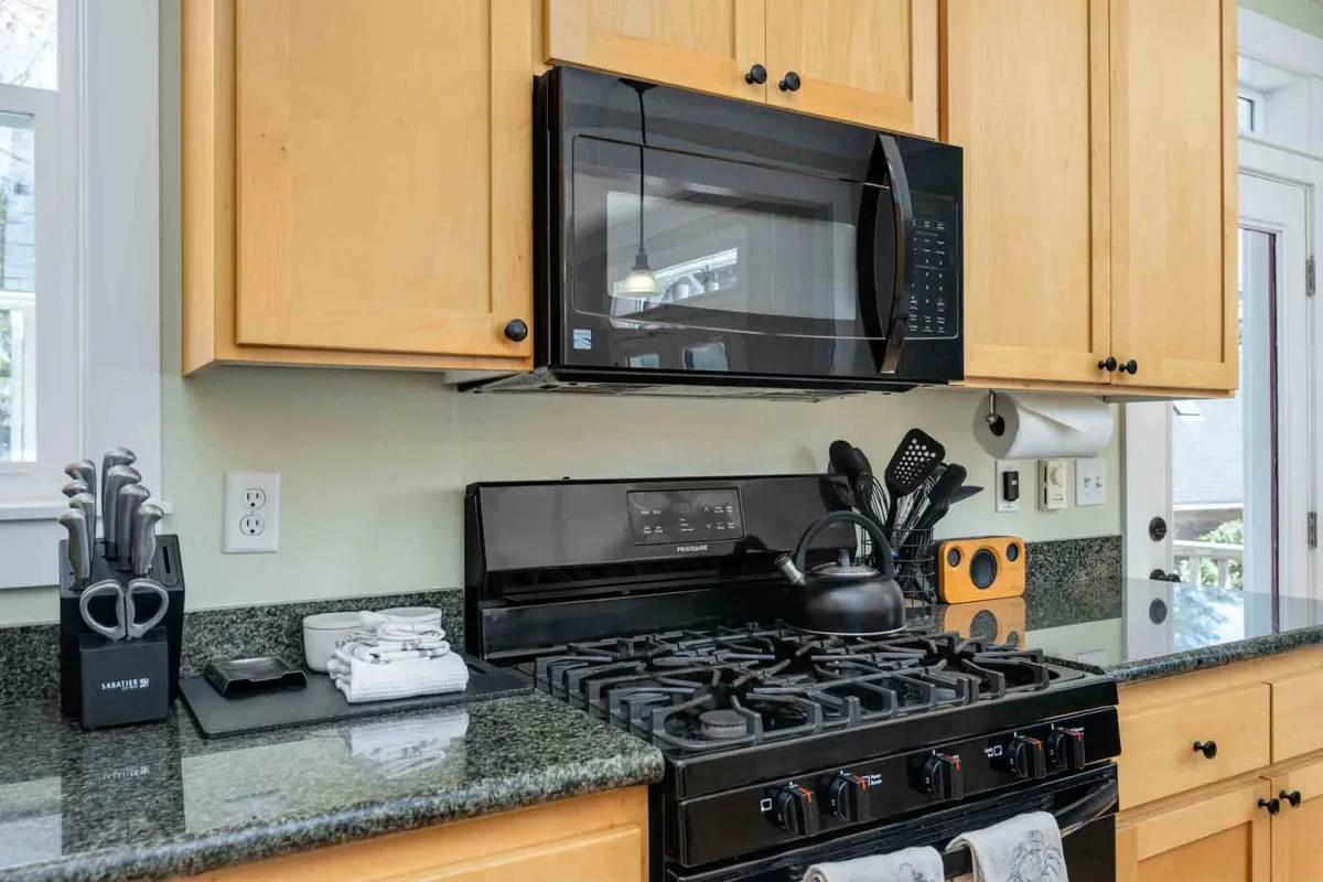 A cozy kitchen scene highlighting a black stove, microwave, kitchen utensils, wooden cabinets, and ample countertop space. The setup suggests a functional and family-friendly environment, ideal for preparing anything from nourishing breakfasts to elaborate dinners. Subtle details like accessible utensils and inviting lighting create a homely atmosphere.