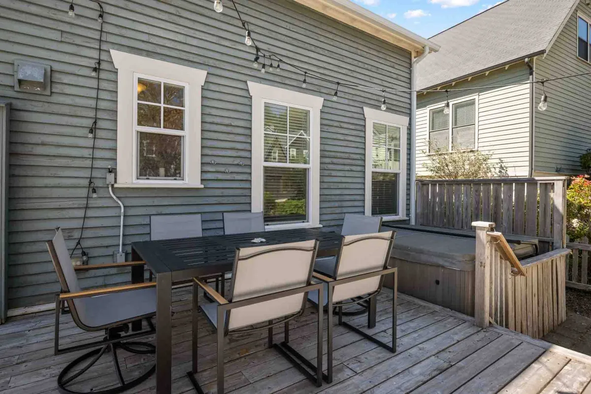 An inviting outdoor dining table sits on a wooden deck, with glowing string lights overhead creating a welcoming atmosphere for group gatherings. The setup suggests both casual daytime meals and cozy evening conversations.