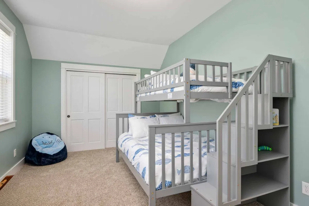 A cheerful bunk room with a sturdy bunk bed, soft carpet underfoot, a bean bag chair for lounging or reading, and closet doors for convenient storage. The space feels playful yet restful, ideal for children.